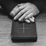 maos sobre biblia na mesa de madeira